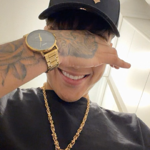 Optical sonriendo con gorra, reloj dorado y cadena