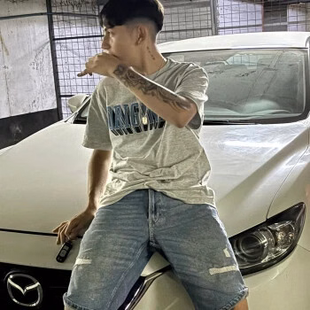 Optical apoyado en el capó de un auto blanco, con polera gris y jeans